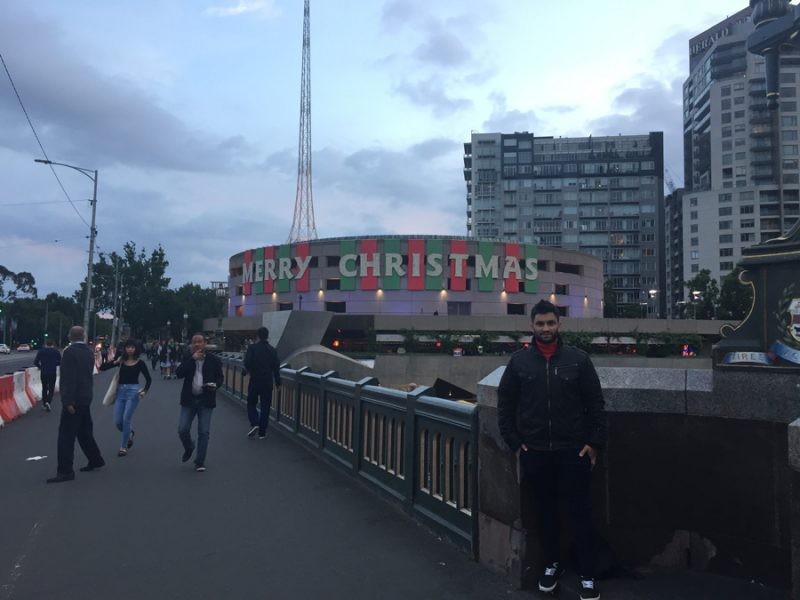 estudiante chico posando delante de un monumento en Melbourne y de fondo el cielo nublado